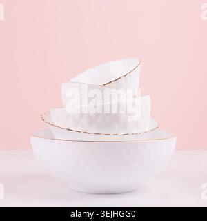 Weißes Keramikgeschirr mit dünner Goldlinie, Texturen in elegantem, hellrosa Interieur auf weißem Holztisch, quadratisch. Luftiges Delikatessen Stockfoto