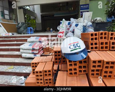 Baustelle mit Stapeln von orangen Tonziegeln und verpackten Materialien, weißem Schutzhelm mit blauer Krempe und CSG-Logo, Ho Chi Minh City, Vietnam Stockfoto