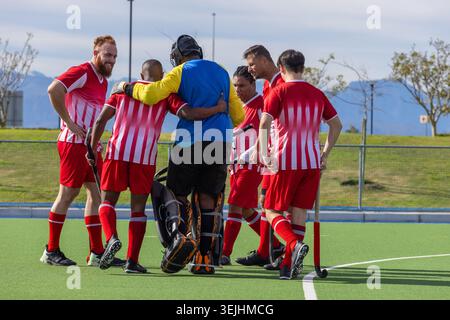 Verschiedene männliche Feldhockeykollegen drängen sich mit Polstern um den Torwart und halten Stöcke auf dem Rasen. Athleten, Teamwork, Kameradschaft Stockfoto