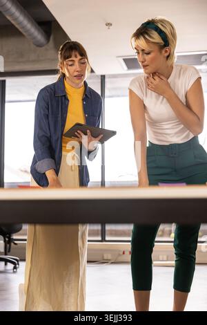 Weibliche Kollegen arbeiten am Schreibtisch zusammen, während sie Tablets und Haftnotizen untersuchen. Zusammenarbeit, Teamarbeit, Innovation, Modus Stockfoto