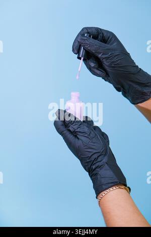 Frau hält Handschuhe in der Hand, die lila nagellackflasche vor blauem Hintergrund hält Stockfoto