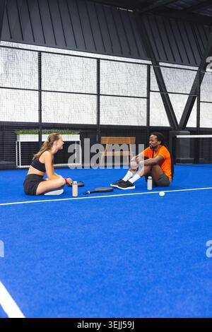 Verschiedene Fitnesspartner in Sportbekleidung auf dem Platz mit Wasserflaschen und Tennisausrüstung. Athleten, Teamwork, Wellness, o Stockfoto
