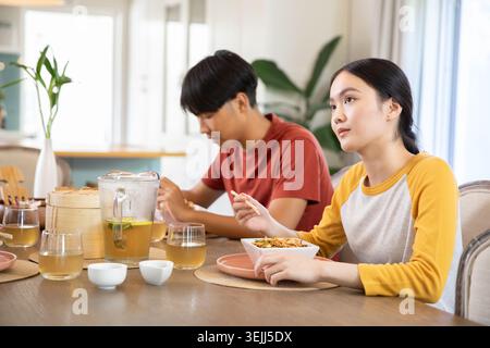 Asiatische Paare sitzen an einem hölzernen Esstisch in der Küche ihres Hauses, essen mit Essstäbchen und trinken Eistee. Paare Stockfoto