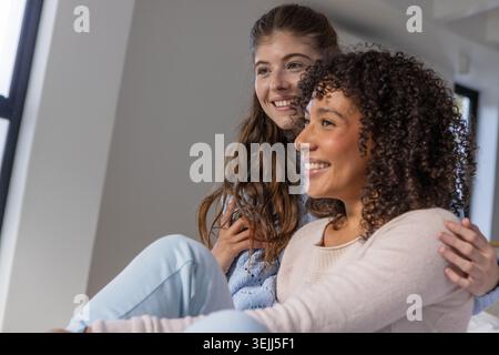 Verschiedene Freundinnen sitzen auf dem Sofa im Wohnzimmer, lächeln und schauen nach rechts. Freundschaft, Kameradschaft, wa Stockfoto