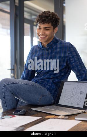 Afroamerikaner sitzt an einem Zeichentisch in einem Studio und liest Skizzen, Stoffmuster, Telefon und Laptop. Kreativ, des Stockfoto