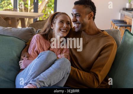 Verschiedene Paare sitzen dicht auf Sofa im Wohnzimmer durch großes Fenster und dekorative Kissen. Romantisch, intim, gemütlich, modern, Stockfoto