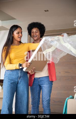 Verschiedene gerahmte Bilder für Paare, die im Wohnbereich mit Luftpolsterfolie und Umzugskartons auspacken. Wohnen, emotional, zwanglos, M Stockfoto