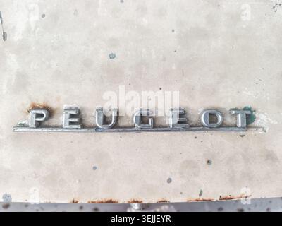 Vintage-Peugeot-Schriftzug von einem Oldtimer. Dieses verchromte Metall-Emblem wurde häufig auf den Frontgittern oder Heckdeckeln klassischer Modelle verwendet. Er ist am bekanntesten an Autos aus den späten 1960er und 1970er Jahren zu sehen Stockfoto