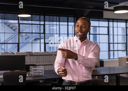 Afroamerikanischer Mann, der bei der Präsentation des Projekts im Großraumbüro mit Drehstühlen Gesten gibt. Modern, professionell, Corporate, Stockfoto