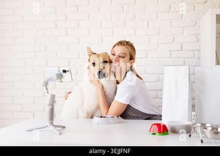 Junge kaukasische Bloggerin, die vor die Kamera schaut, mit ihrem Hund gestreamt Stockfoto