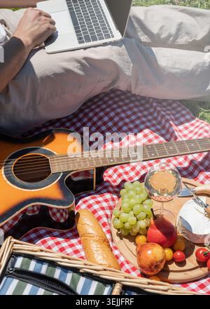 Unerkennbarer Mann in weißer Hose draußen, der Picknick macht und Laptop benutzt, draußen arbeitet Stockfoto