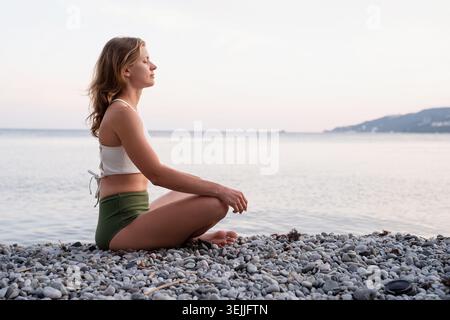 Junge Frau meditieren am Strand Stockfoto