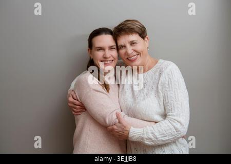 Glückliche Seniorenmutter und erwachsene Tochter, die auf grauen Hintergrund in die Kamera schauen Stockfoto