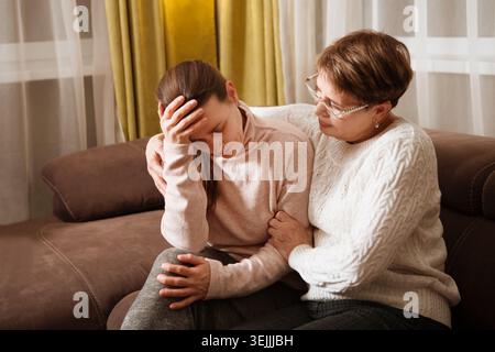 Ältere Mutter Konsolen, tröstende traurige Erwachsene Tochter, die zu Hause auf dem Sofa sitzt. Unterstützung bei zwei Altersgenerationen Stockfoto