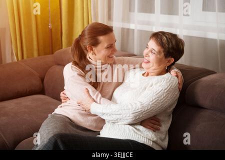 Glückliche Seniorin Mutter und Erwachsene Tochter umarmen sich drinnen. Familienzeit. Stockfoto