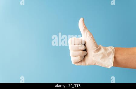Die Hand trägt einen weißen Gummihandschuh, der die Daumen nach oben zeigt. Stockfoto