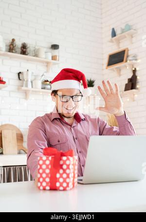 Glücklicher junger Mann mit weihnachtsmann, der seine Freunde im Videochat begrüßt oder auf dem Laptop anruft Stockfoto