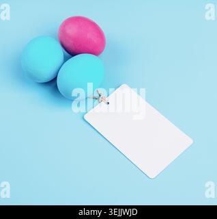 Farbige Eier mit leerem weißen Etikett isoliert auf blauem Hintergrund Draufsicht Stockfoto