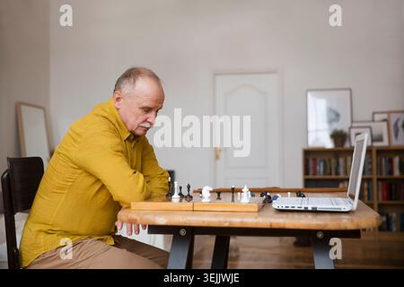 Älterer alter Mann spielt Schachspiel auf Schachbrett, Online-Spiel mit einem Freund, Videoanruf wegen sozialer Distanz zu Hause Stockfoto