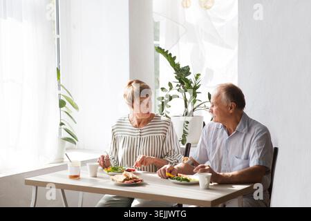 Porträt eines entspannten, spaßigen Seniorenpaares zusammen und beim Frühstück in der Küche zu Hause Stockfoto