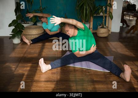 Aktives Seniorenpaar, das zu Hause Dehnübungen und Yoga macht. Fitness zu Hause, Aktivkleidung. Gesunder und sportlicher Lebensstil. Stockfoto