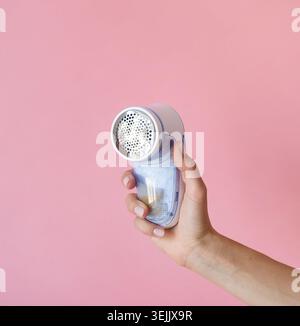 Weibliche Hand, die Anti-Pilling-Rasierer-Maschine auf rosa Hintergrund hält Stockfoto