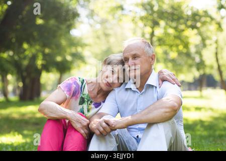 Glückliches älteres Ehepaar, das zusammen auf Gras sitzt und sich im Garten entspannt. Stockfoto