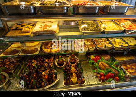 Eine gekühlte Vitrine gefüllt mit einer Vielzahl von süßen Gebäckstücken, Kuchen und herzhaften zubereiteten Speisen Stockfoto