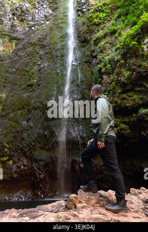 Wanderer genießen einen natürlichen Wasserfall und üppige grüne moosbedeckte Klippen während der Erkundung der Natur Stockfoto