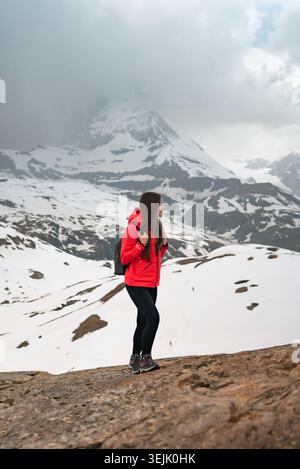 Frau, die auf Felsen steht und die schneebedeckte Berglandschaft unter bewölktem Himmel genießt Stockfoto