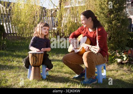 Glückliche Familie Mutter und Tochter, die Spaß mit Musikinstrumenten haben, singen auch gemeinsam Lieder im Freien. Mom spielt Gitarre und Stockfoto