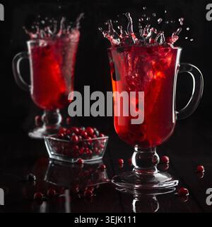 Leuchtend roter Glühwein mit Beeren und Spritzer in zwei Glas Weingläser im schwarzen dunklen Innenraum, quadratisch. Stockfoto