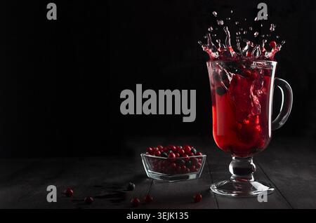 Leuchtend roter Glühwein mit Beeren und Spritzer in Glas Weinglas auf schwarzem Holztisch im dunklen Innenraum, Kopierraum. Stockfoto