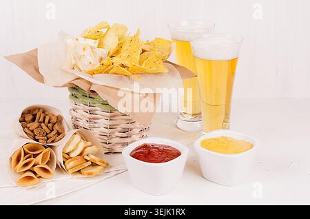 Goldene bunte Snacks - Nachos, Popcorn, Croutons, Chips im rustikalen Korb und Bastelpapierkegel und Saucen in der Schüssel, Lagerbier usw. Stockfoto