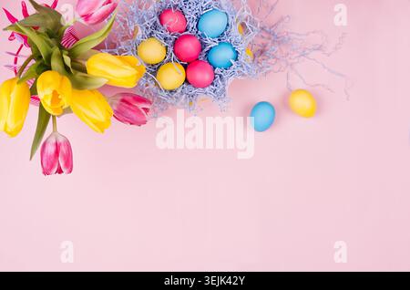 Sanfte elegante, weiche osterdekoration in Pastellfarben - bemalte Eier, gelbe Tulpen, Cupcake auf rosa Hintergrund, Kopierraum, Draufsicht. Stockfoto