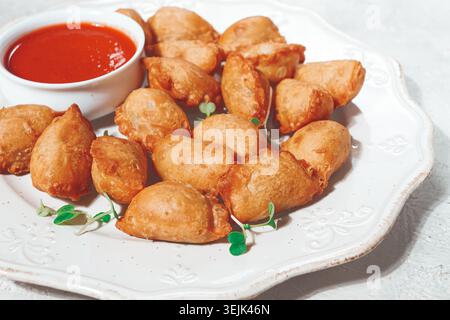 Gebratene Mini-Chebureks, mit Sauce, auf einem dekorativen Teller, hartes Licht, keine Leute, Stockfoto