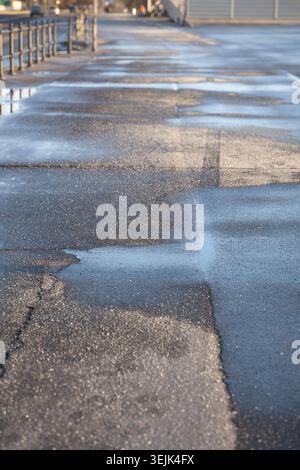 Enteisungsmittel auf Asphalt im Winter. Salzkörner auf eisiger Bürgersteig-Pflasterplatte mit technischem Salz Stockfoto