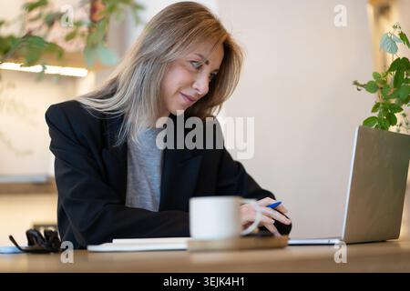 Lächelnde Geschäftsfrau, erfolgreiche Managerin, die in der Mittagspause an der Fernbedienung im Café mit Laptop arbeitet. Stockfoto