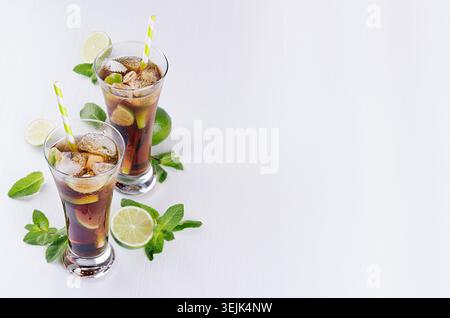 Sommerfrischer Cola-Cocktail mit Eis in zwei Gläsern mit Minze und Limette als Rand auf weißem Holzbrett, Blick von oben. Stockfoto