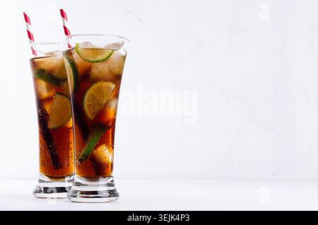 Kalter Cocktail cuba libre in zwei langen Gläsern mit Strohhalm, Stücke Limette auf weichem, modernem weißem Hintergrund. Stockfoto