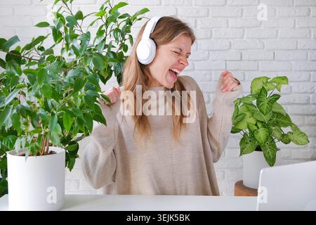 Millennials-Frau, die einen Laptop für die Arbeit benutzt, zu Hause am Tisch sitzt und gute Nachrichten hat Stockfoto