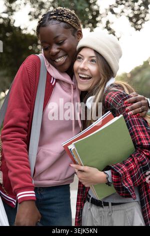 Verschiedene junge Schülerinnen stehen auf baumgesäumten Pfaden, beugen und lächeln, halten Notizbücher. Freunde, Campus, Outdoor, Falten Stockfoto