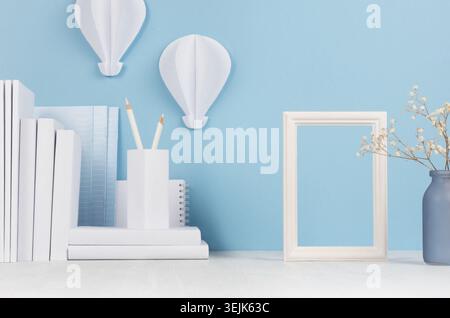 Moderner Heim-Arbeitsplatz - weiße Schreibwaren, leerer Rahmen, Blumen auf weichem blauem Hintergrund und heller Schreibtisch. Stockfoto