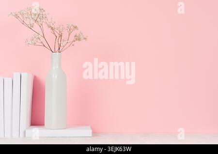 Romantische Inneneinrichtung mit weißen trockenen Blumen in Vase und weißen Büchern auf hellrosa Hintergrund. Stockfoto