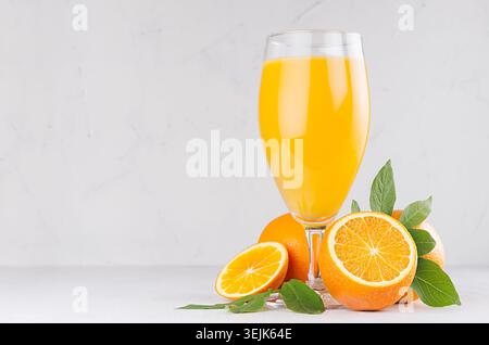 Gesunde hausgemachte Limonade - Orangensaft im Weinglas mit Orangen und grünen Blättern auf weißem Holzhintergrund. Stockfoto