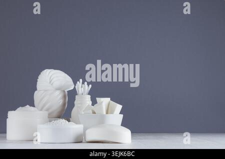 Weiße Kosmetikprodukte in verschiedenen weißen Schalen auf Holztisch und grauer Wand mit Kopierraum. Stockfoto