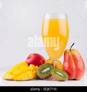 Tropischer Fruchtsaft in elegantem Glas mit verschiedenen Früchten auf weißem Holzbrett, quadratisch. Stockfoto