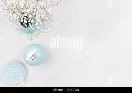 Badezimmeraccessoires in zarten pastellblauen Keramikformen und kleinen weißen Blumen auf weißem Holzbrett, Draufsicht, Kopierraum Stockfoto