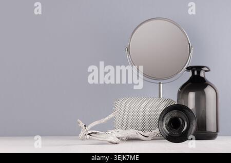 Minimalistisches Innenbadezimmer in monochromer Grau - schwarze Glasvase, Spiegel, Kreis, alte Schlinge, silberne Kosmetiktasche auf weiß Stockfoto