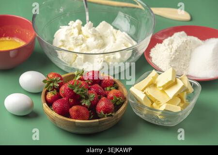 Frische Backzutaten, einschließlich Erdbeeren, Butter, Zucker und Quark, auf grünem Hintergrund Stockfoto